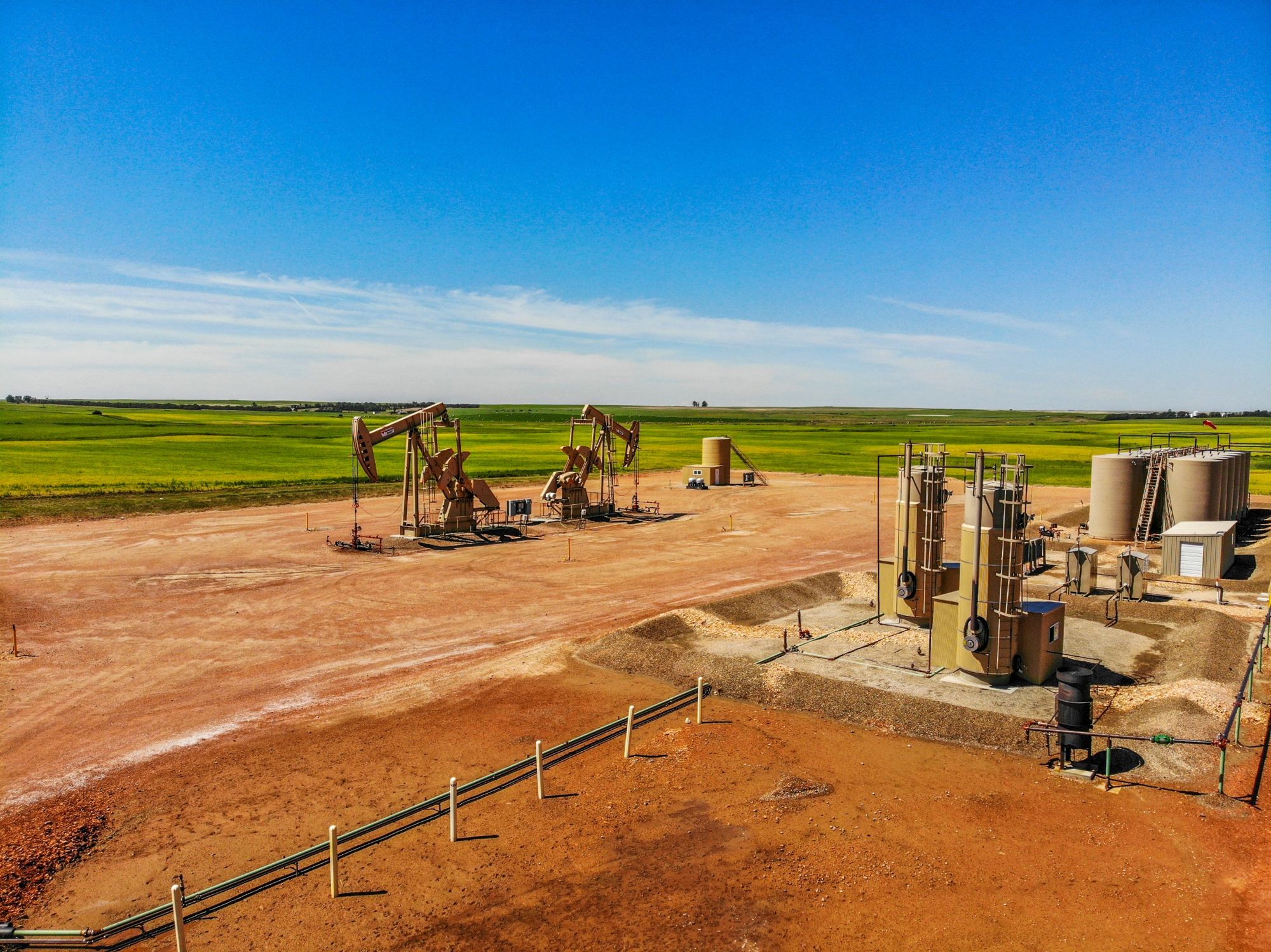 Aerial view of a well pad with pumpjacks and tanks on red scoria